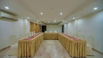 Un salón de conferencias con una larga mesa, sillas blancas y un aire acondicionado instalado en el techo.