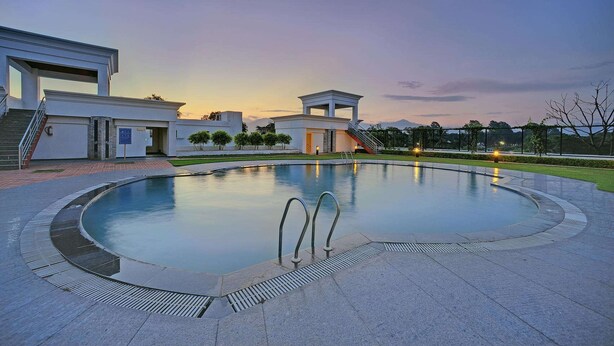 A modern pool area with a clear sky, a well-maintained lawn, and a building with a flat roof and large windows. - Royal Sarovar Portico Siliguri (Jalpaiguri)