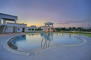 A modern pool area with a clear sky, a well-maintained lawn, and a building with a flat roof and large windows. - Royal Sarovar Portico Siliguri (Jalpaiguri)