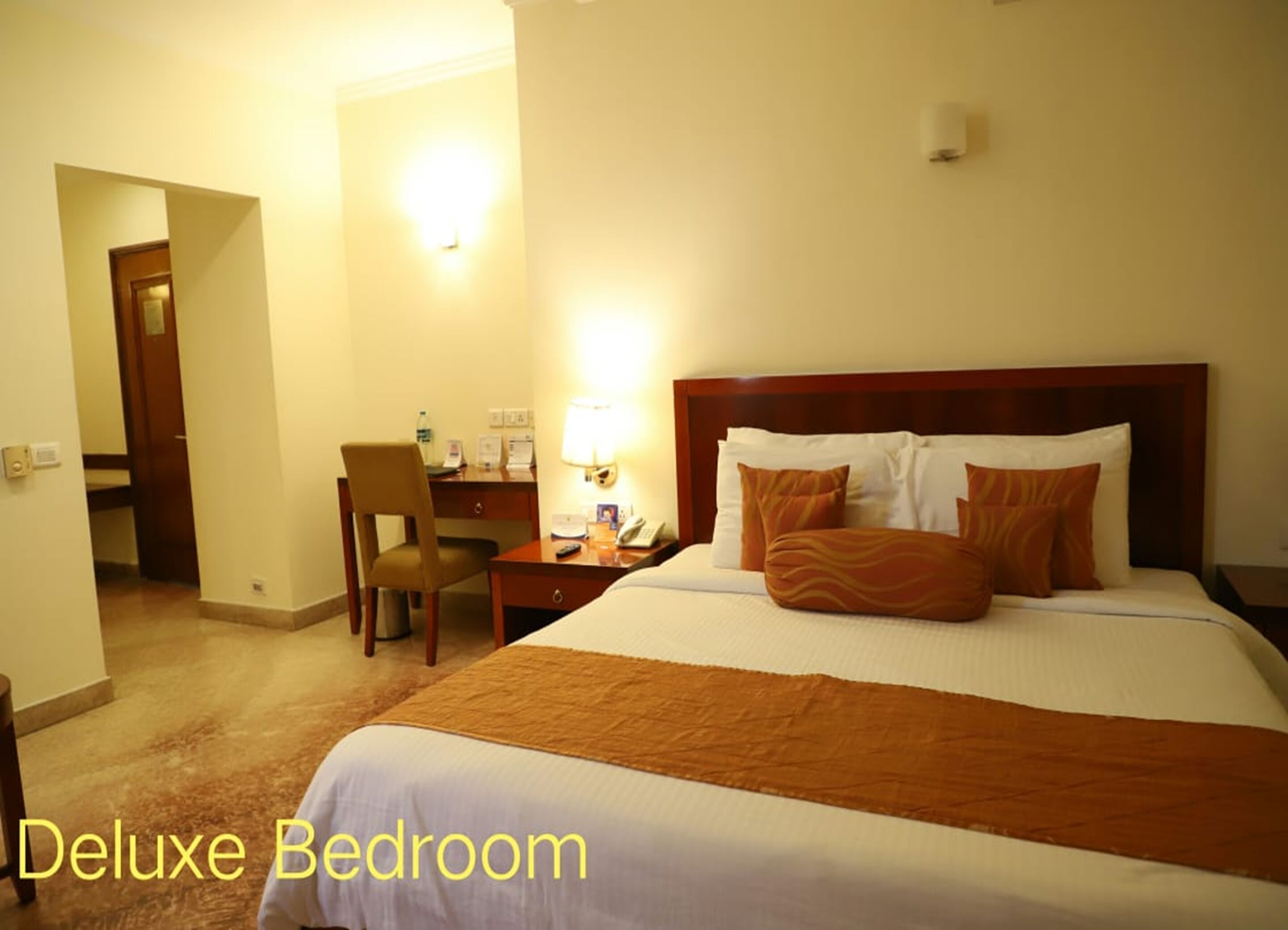 A Deluxe Bedroom with a large bed, two pillows, a desk with a chair, a lamp, and a nightstand.