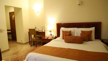 A Deluxe Bedroom with a large bed, two pillows, a desk with a chair, a lamp, and a nightstand.
