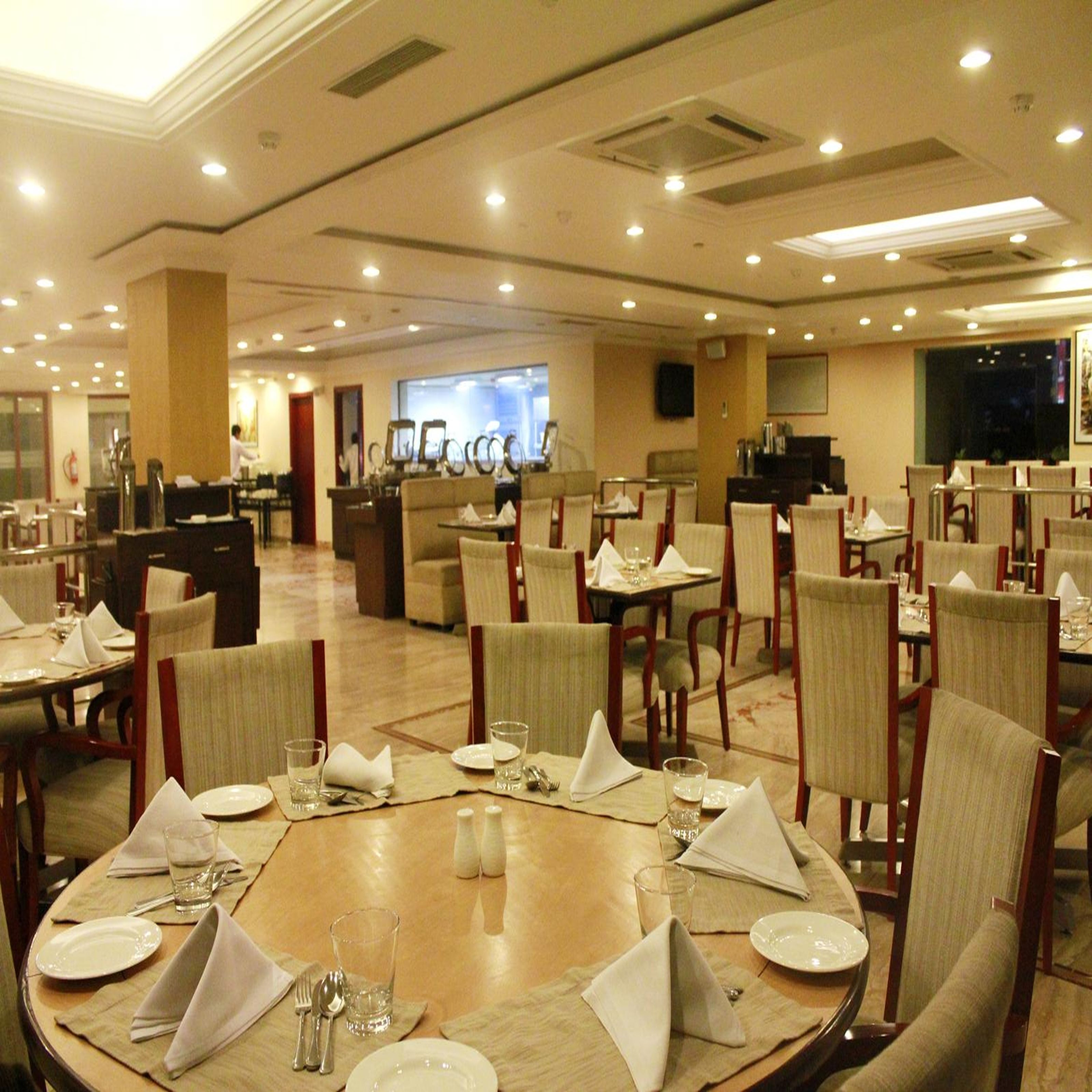 A spacious restaurant with multiple dining tables, chairs, and a large screen in the background.