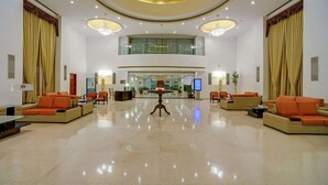 A spacious lobby with a high ceiling, large windows, and a central reception desk. - Royal Sarovar Portico Siliguri (Jalpaiguri)
