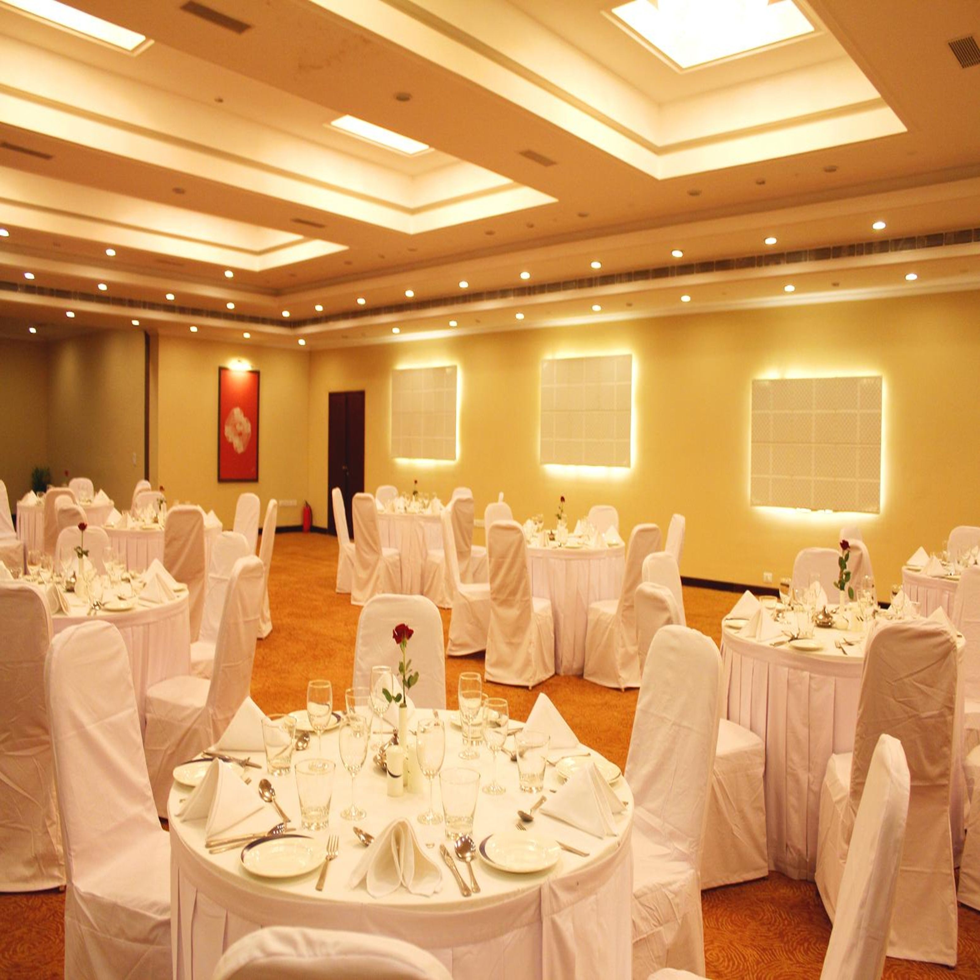 Un salón de banquetes con mesas redondas dispuestas para comer, sillas blancas e iluminación empotrada en el techo.