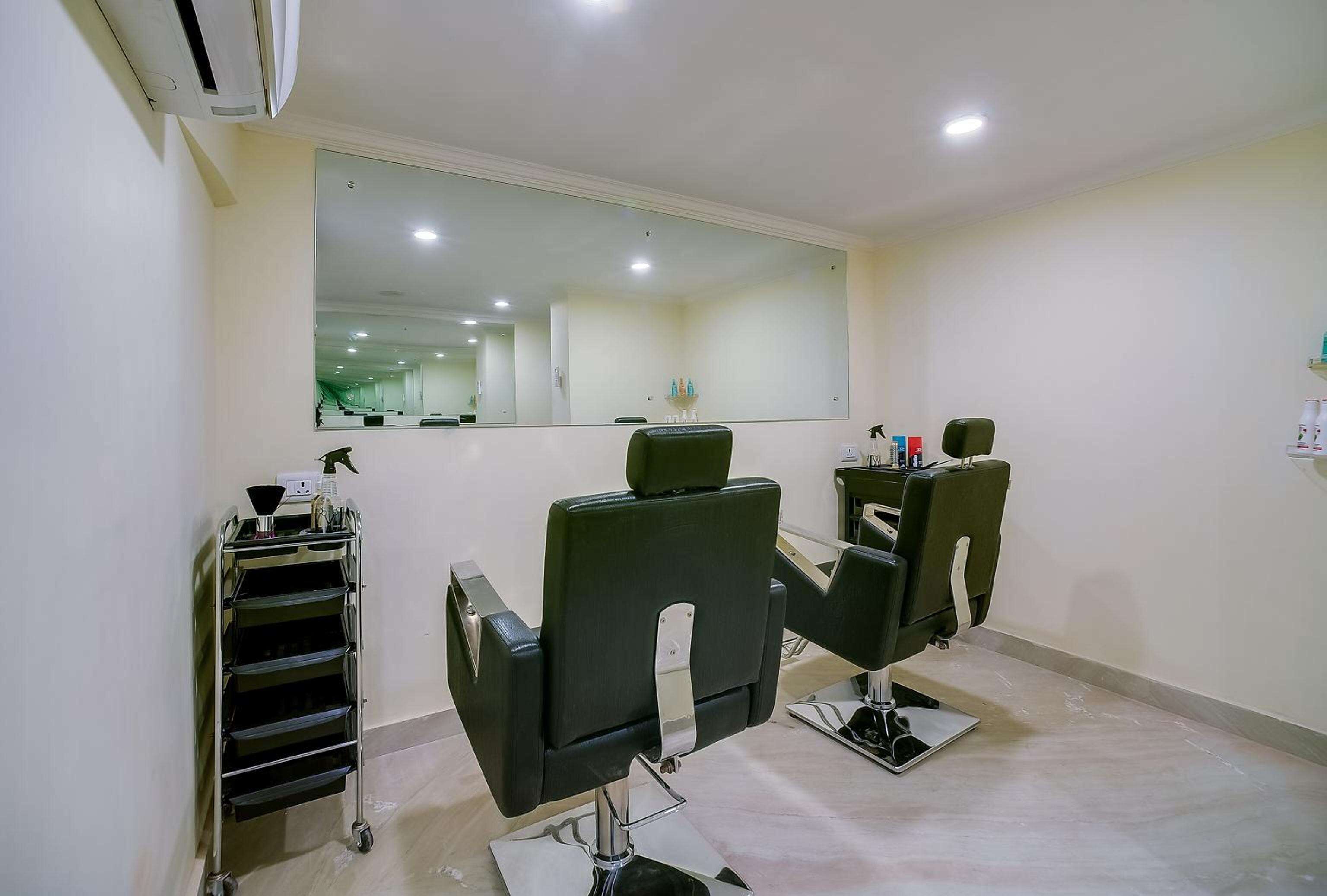 A salon with two black salon chairs, a large mirror, and a metal cart with trays.