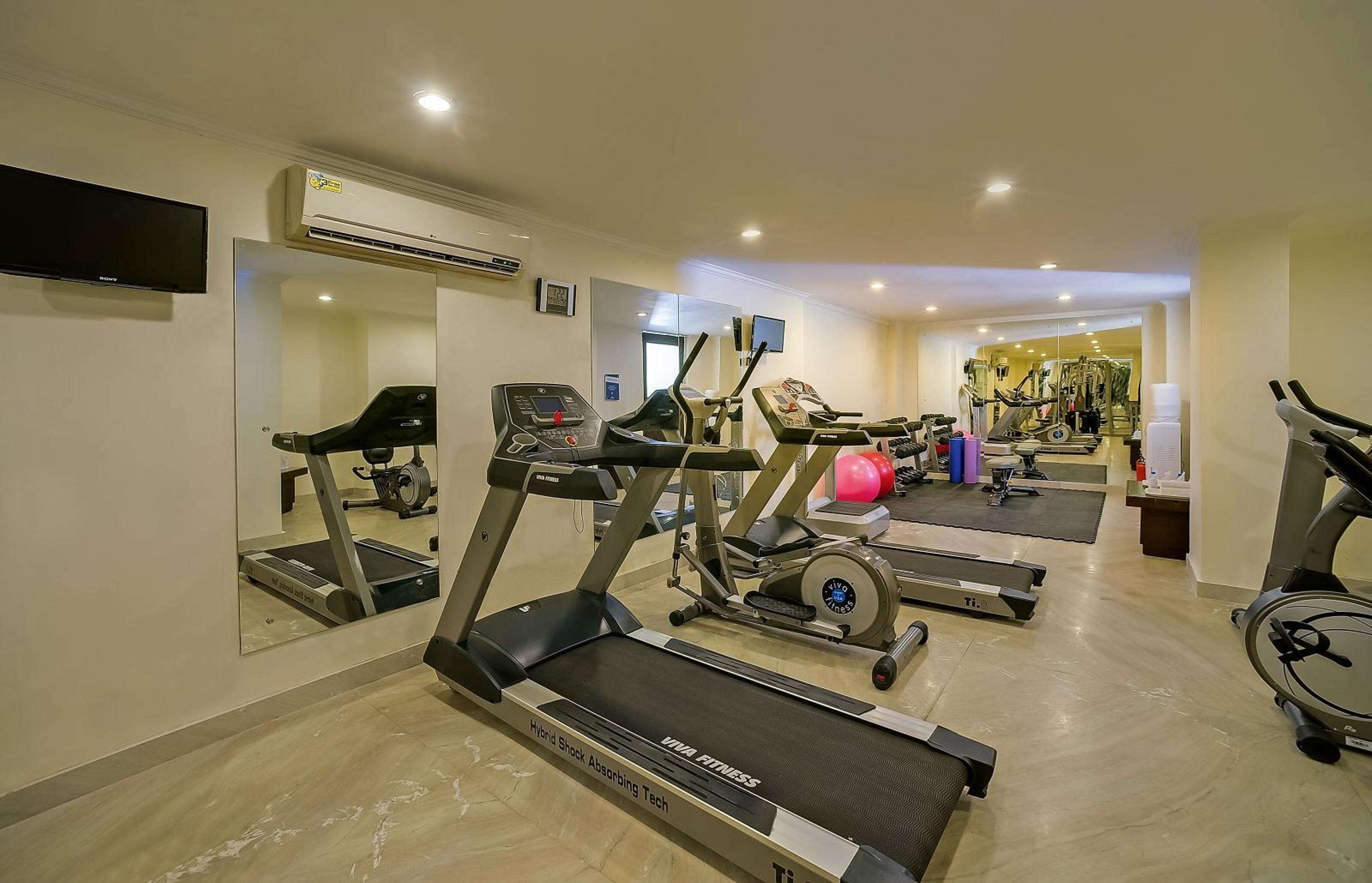 Une salle de sport équipée de tapis de course, de vélos elliptiques et d’un mur recouvert de miroirs.