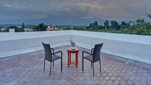 A rooftop terrace with two chairs and a small table, overlooking a cityscape and mountains. - Royal Sarovar Portico Siliguri (Jalpaiguri)