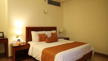 A hotel room with a large bed, a bedside table with a lamp, a phone, and a small table with a picture frame and a book.