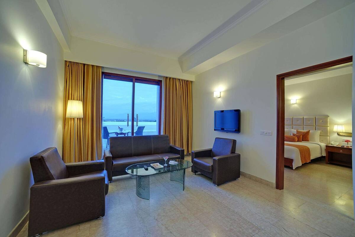 A hotel room with a seating area, a bed, a television, and a view of the sea.