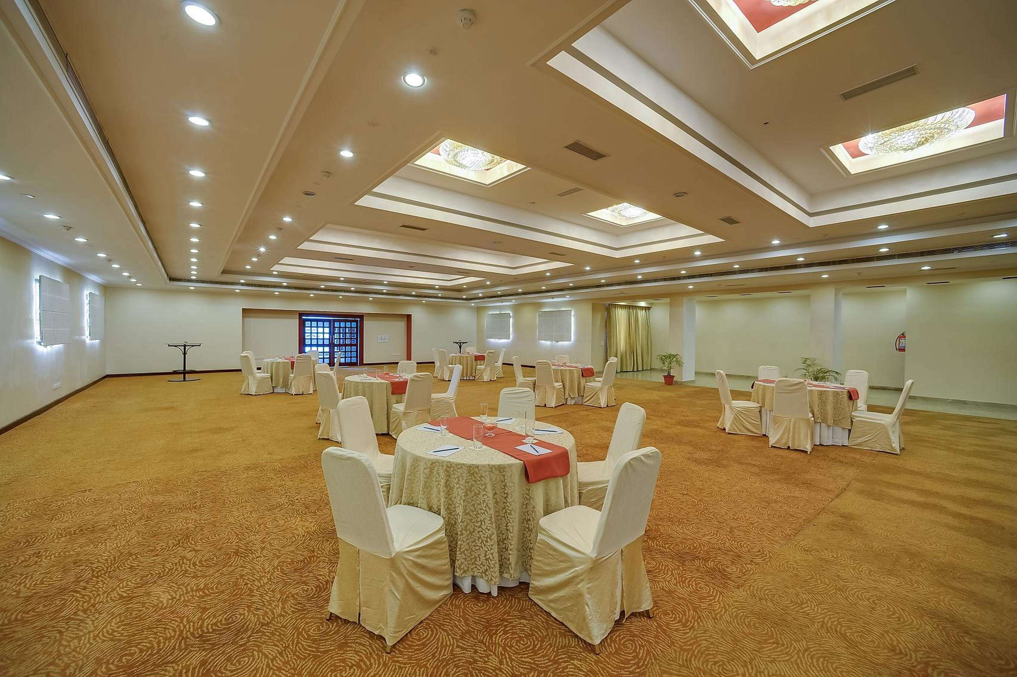 A large conference room with round tables and white chairs, equipped with ceiling lights and skylights.