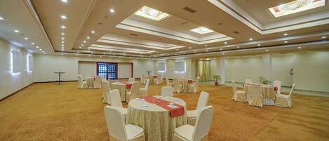 A large conference room with round tables and white chairs, equipped with ceiling lights and skylights.