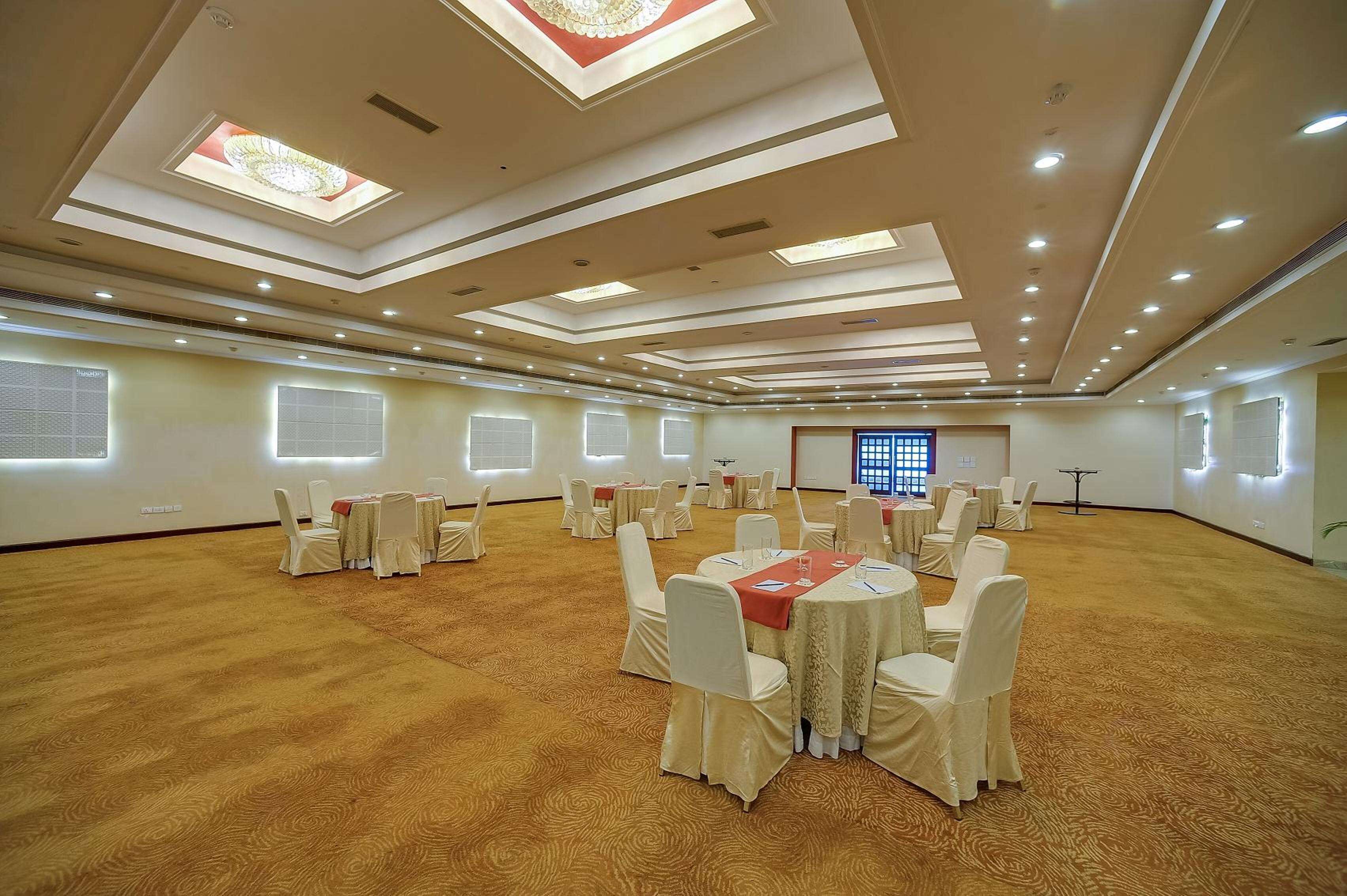 A large conference room with multiple round tables and chairs, recessed lighting, and a patterned carpet.