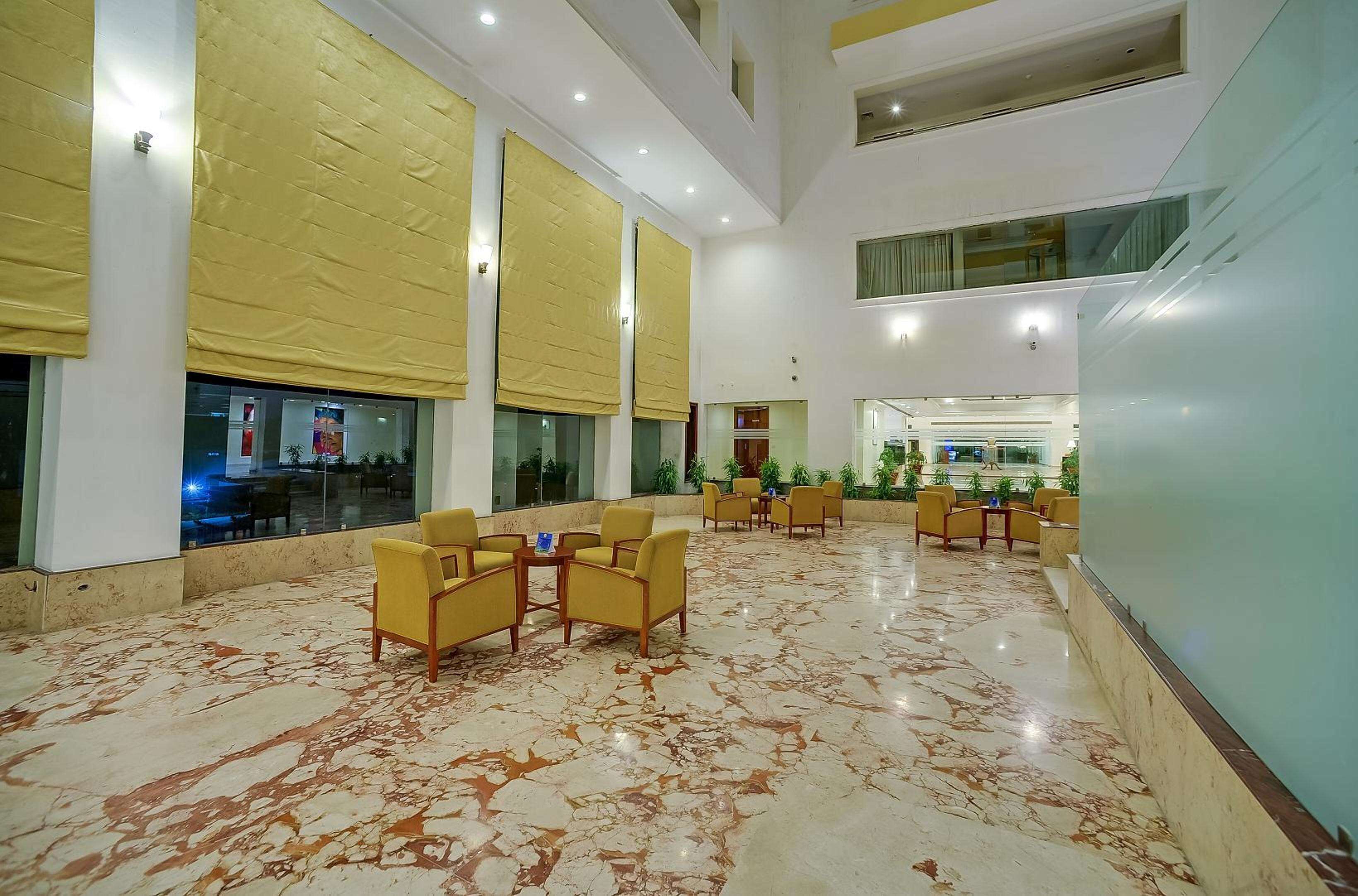 Un hall d’entrée spacieux, doté d’un sol en marbre, de chaises jaunes et de grandes fenêtres équipées de stores jaunes.
