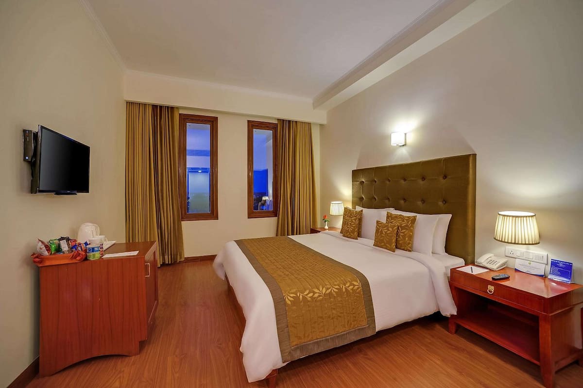 A hotel room with a large bed, a wooden nightstand, a television, and a window with curtains.