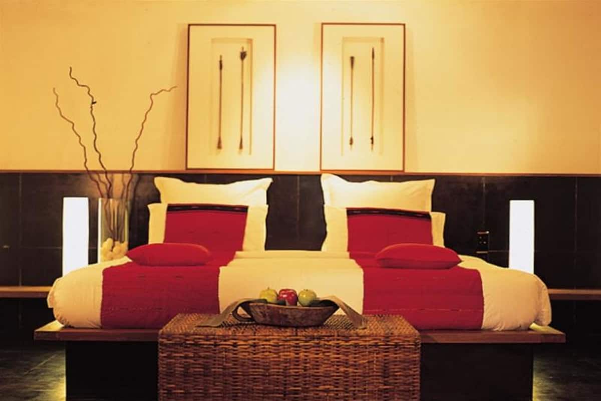 A modern bedroom with a large bed, red and white bedding, a bedside table with fruit, and two framed artworks on the wall.
