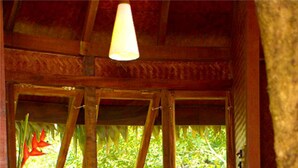 A cozy room with a wooden bench, a red cushioned seat, a wooden chest, and a window with a view of greenery. - Rainforest Boutique Resort (Chalakudy)