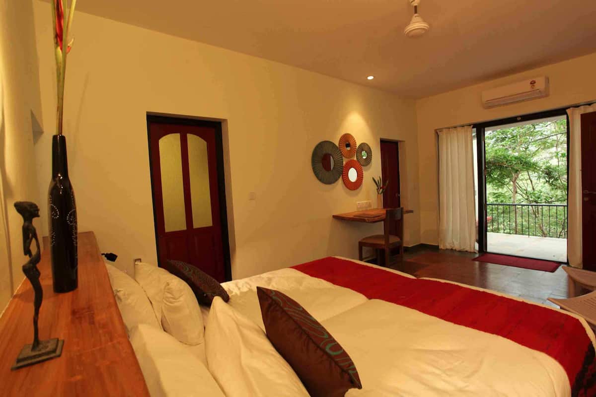 A hotel room with a bed, a wooden table, a vase, a door, a wall decoration, and a balcony with a view.