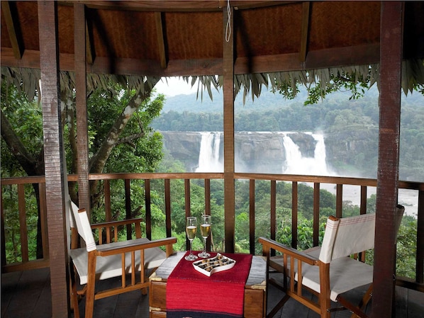 Une terrasse en bois avec deux chaises et une table, d’où l’on peut admirer une cascade.