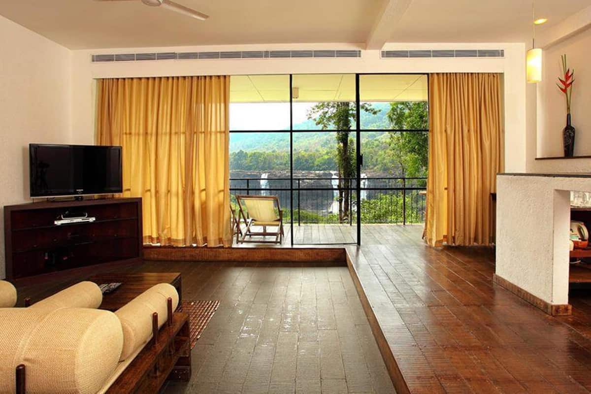 A spacious living area with a flat-screen TV, a sofa, and a balcony with a view of a waterfall.