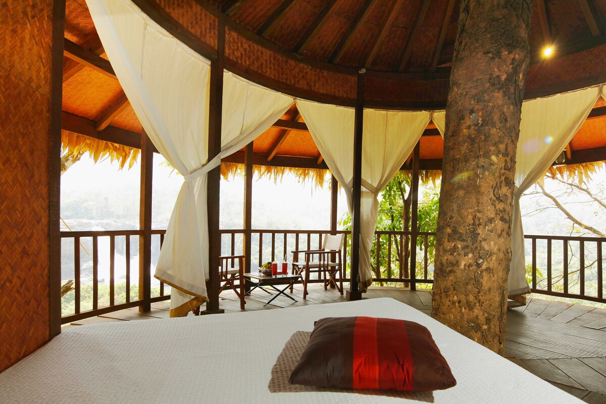 A room with a bed, a table with chairs, and a view of a natural landscape.