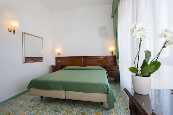 A hotel room with a bed, a nightstand, a mirror, and a potted orchid.