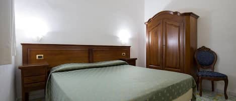 A bedroom with a bed, a wooden wardrobe, a nightstand, and a chair.
