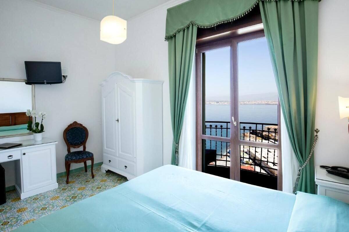 Une chambre d’hôtel équipée d’un lit, d’un bureau, d’une chaise, d’une télévision et d’un balcon avec vue sur la mer.
