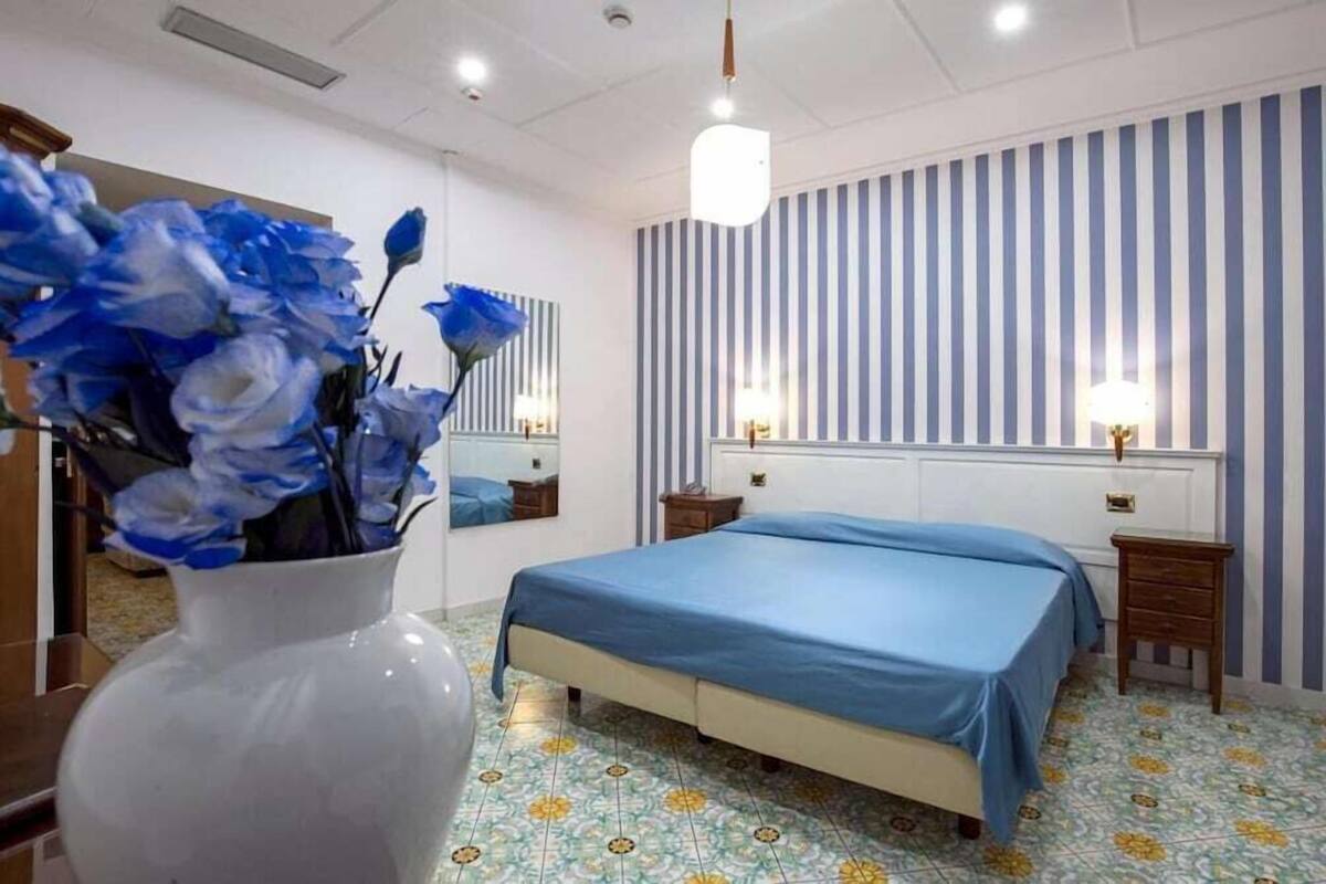 Une chambre à coucher avec un lit, des tables de chevet, un miroir et un vase de fleurs.