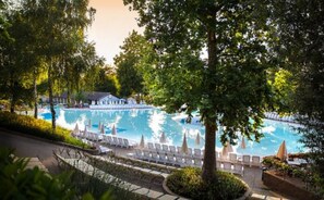 A swimming pool with lounge chairs and umbrellas, surrounded by trees and a building in the background. - hu Altomincio village (Valeggio sul Mincio)