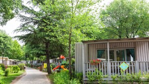 Een pad dat leidt naar een houten chalet met een balkon, omringd door weelderige begroeiing en een speeltuin.