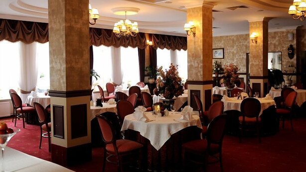 A formal dining room with multiple tables and chairs, elegant chandeliers, and large windows with curtains. - Hotel Chopin (Sochaczew)