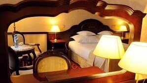 A hotel room with a large mirror, a bed with pillows, a bedside table with a lamp, and a chair. - Hotel Chopin (Sochaczew)