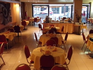 Un restaurante con varias mesas redondas cubiertas con manteles amarillos, sillas rojas y vajilla dispuesta con cuidado.