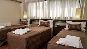 A hotel room with three single beds, each with a brown bedspread and white pillows. There is a bedside table with a lamp on each side of the room. - Hotel Gran Vendimia by Bouquet (Mendoza)