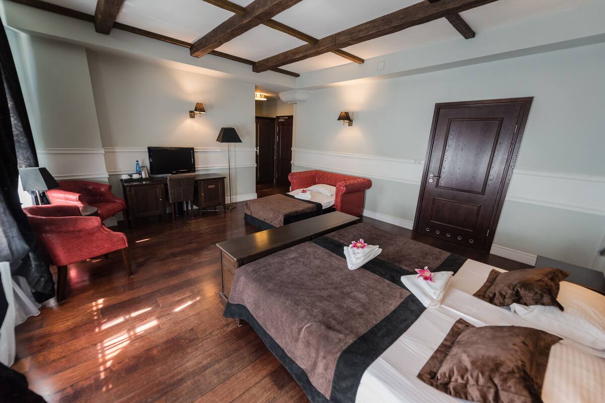 Habitación de hotel con suelo de madera, sofá, cama, televisor y escritorio.