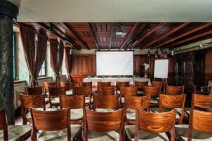 Una sala conferenze con sedie e tavoli in legno, uno schermo di proiezione bianco e un soffitto in legno.