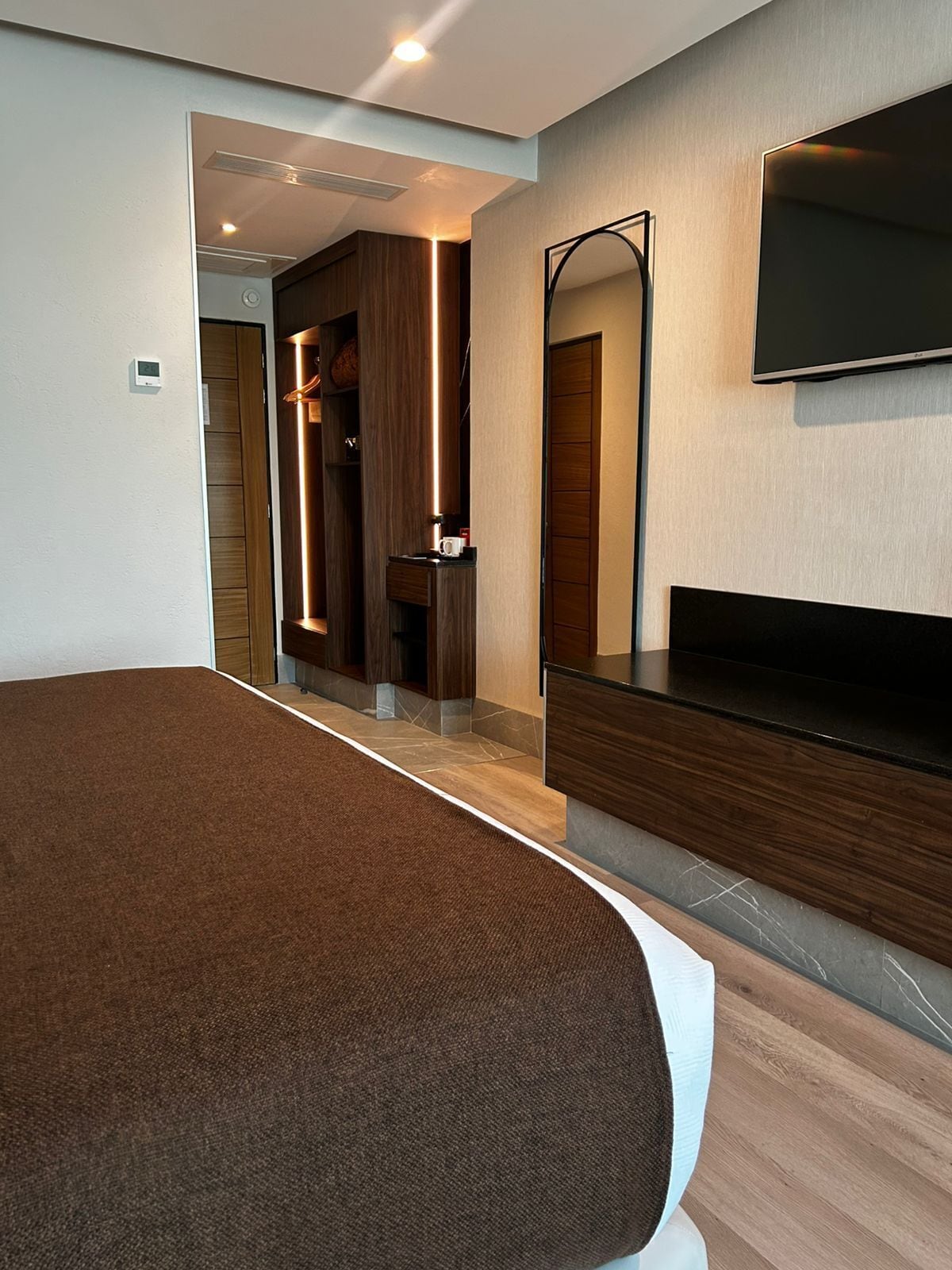 Una camera d'albergo moderna con un letto grande, una TV a schermo piatto, un armadio a muro e uno specchio.