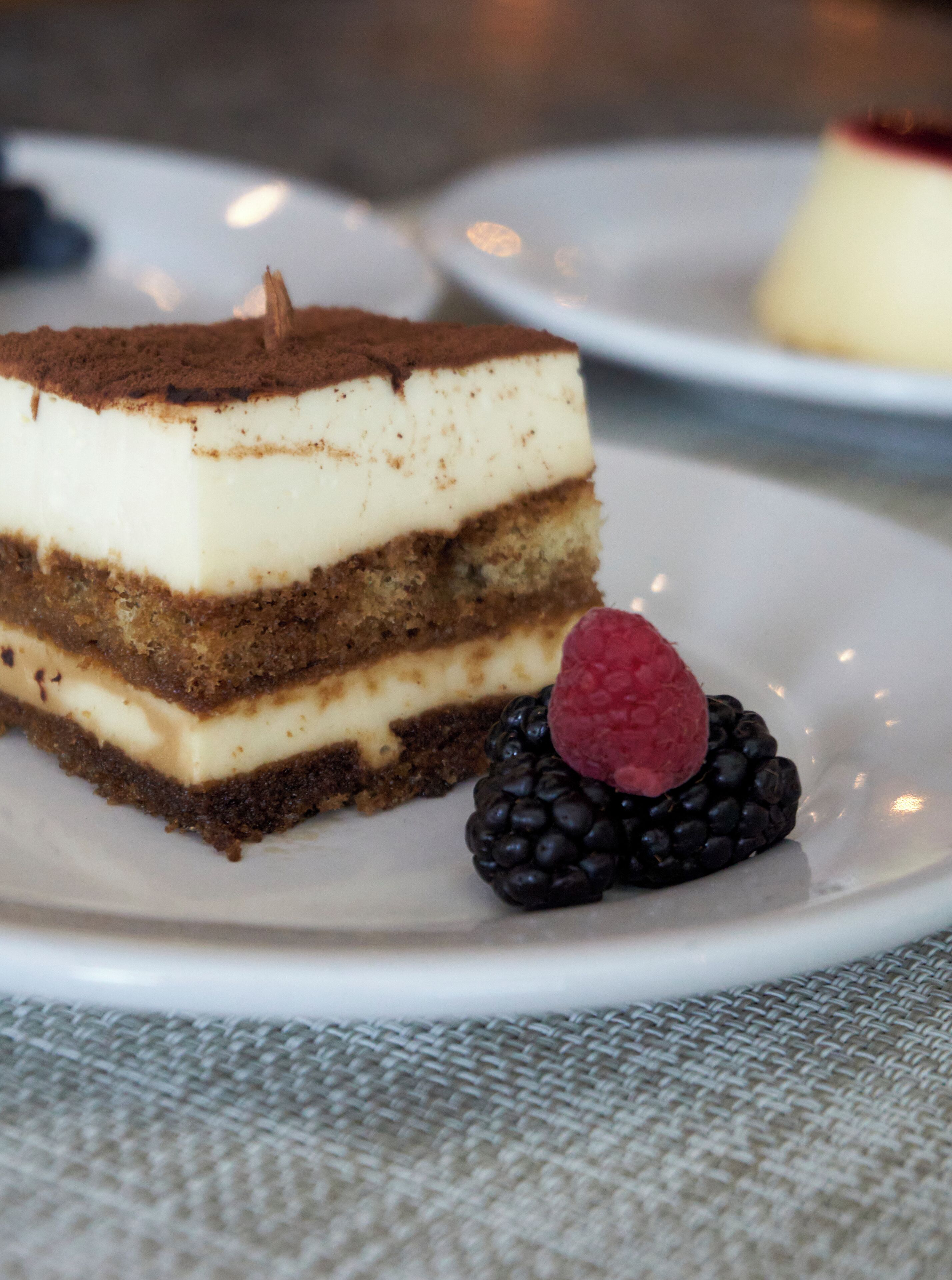 A slice of layered dessert with a raspberry and blackberry on a white plate.