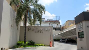 La entrada al Hotel Portobelo, con un camino despejado, palmeras y automóviles estacionados.