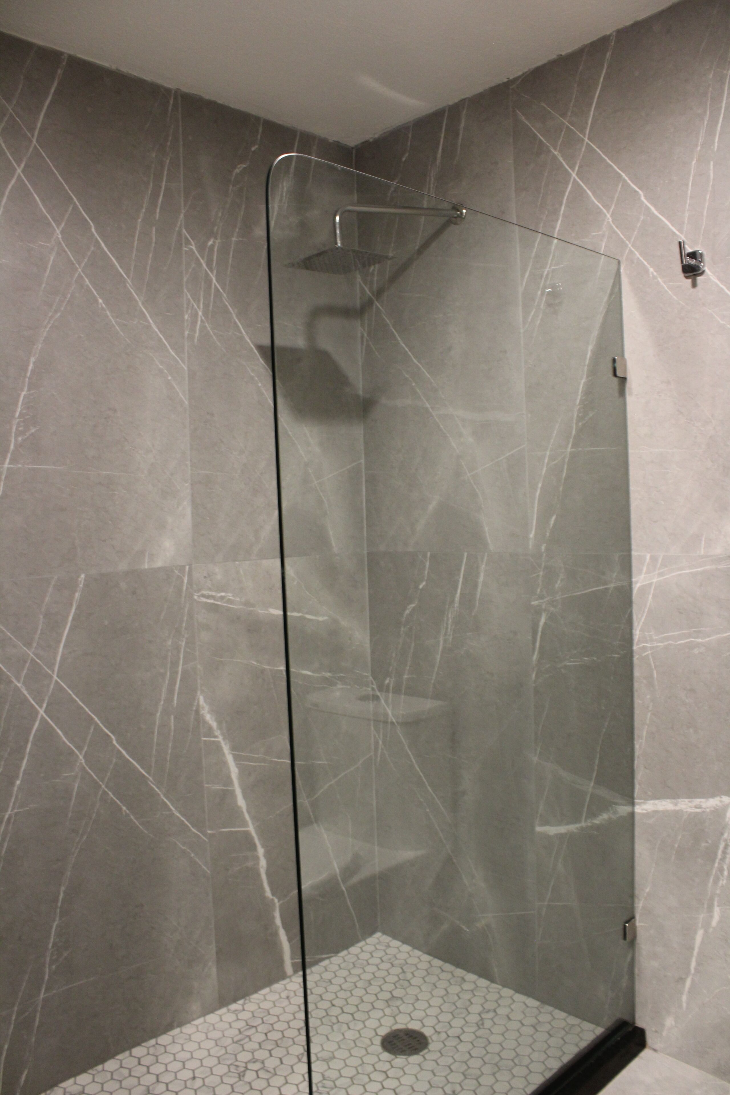Una cabina doccia in vetro con pavimento in piastrelle esagonali e parete con effetto marmo.