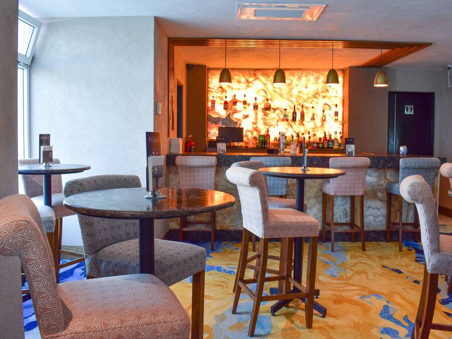 A bar area with round tables and cushioned chairs, a marble wall with a fire-like design, and a patterned carpet.