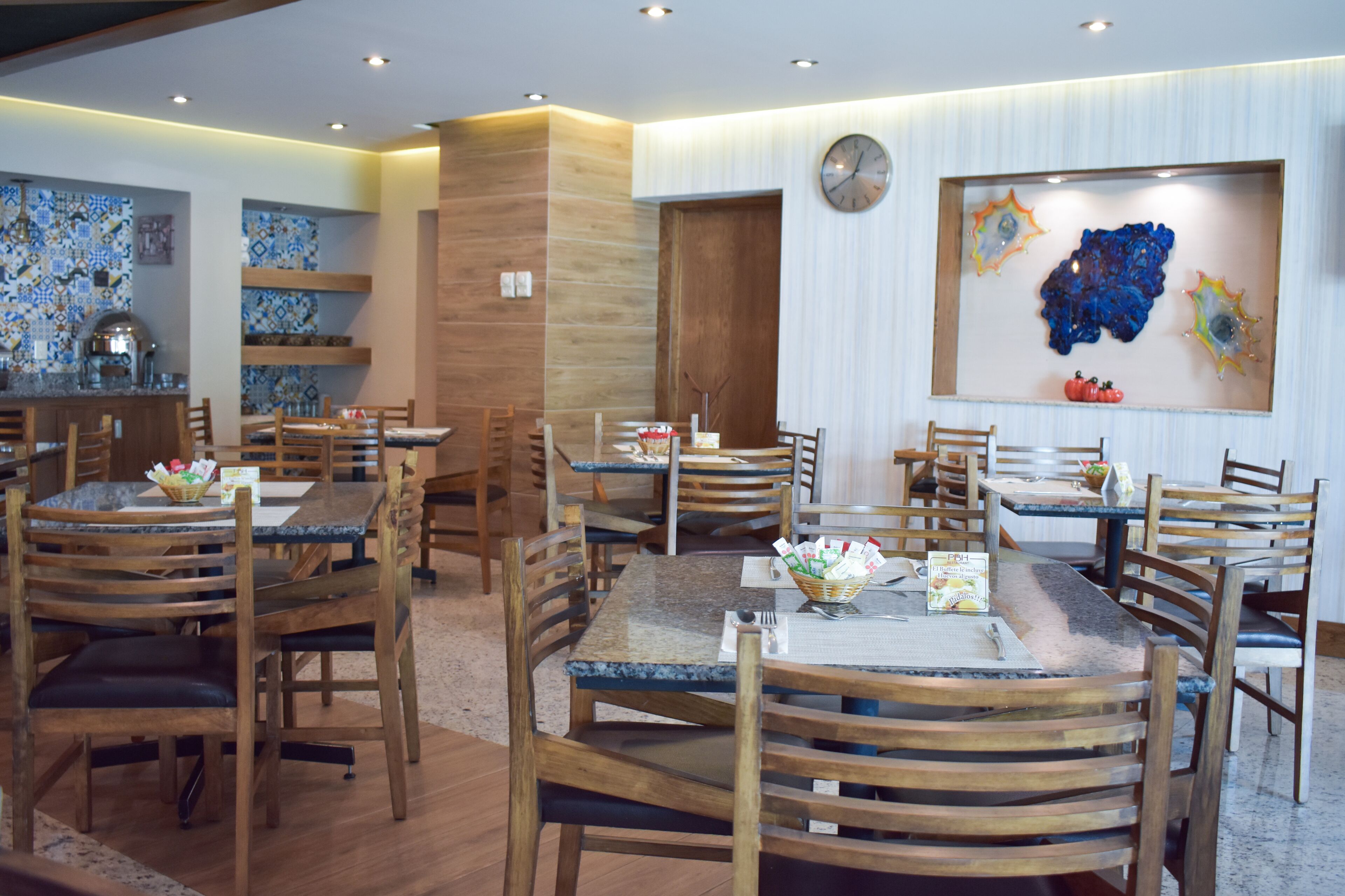Un restaurante con mesas y sillas de madera, un reloj en la pared y decoración artística en las paredes.