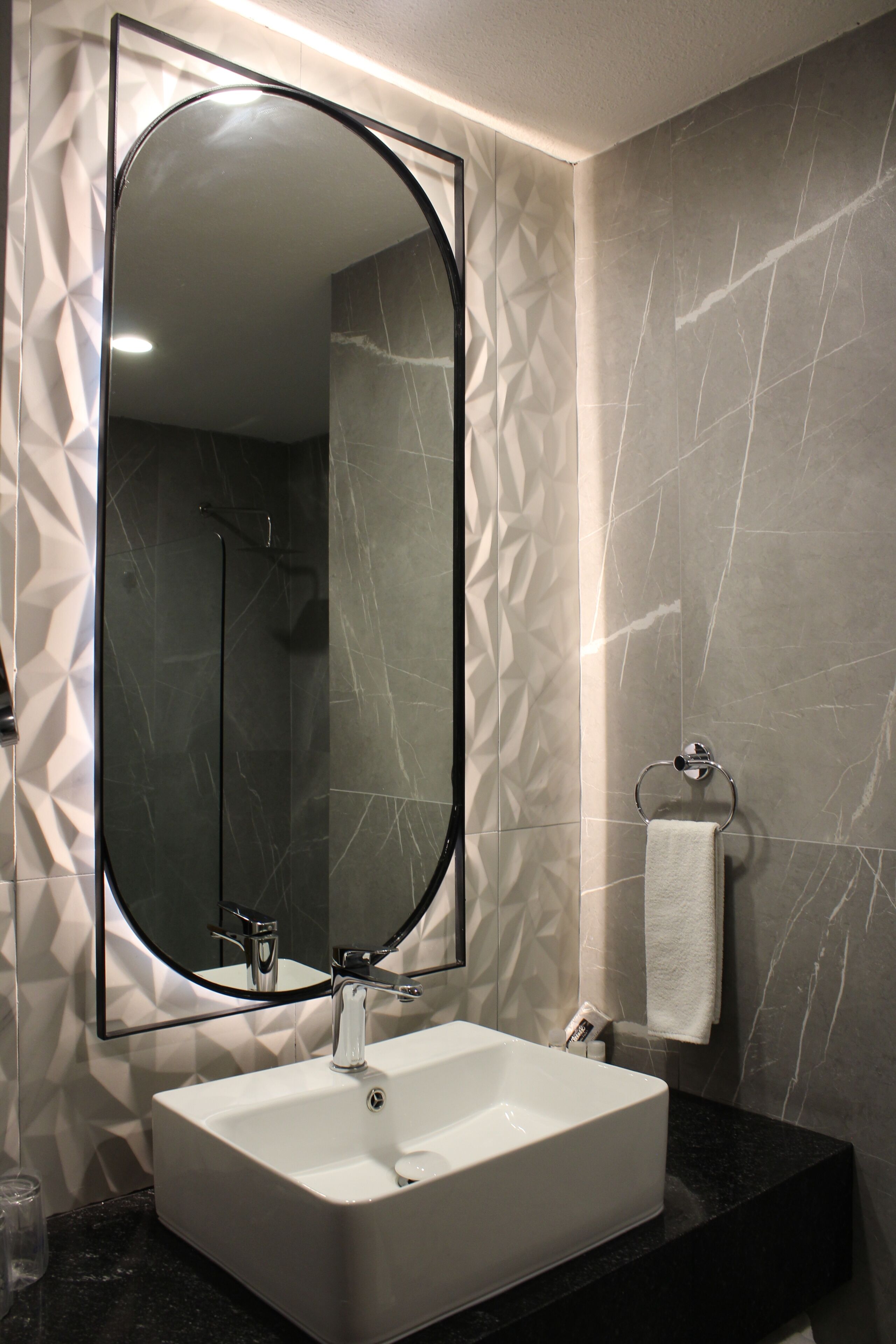 Un baño con un lavamanos rectangular, un espejo grande y un perchero para toallas.