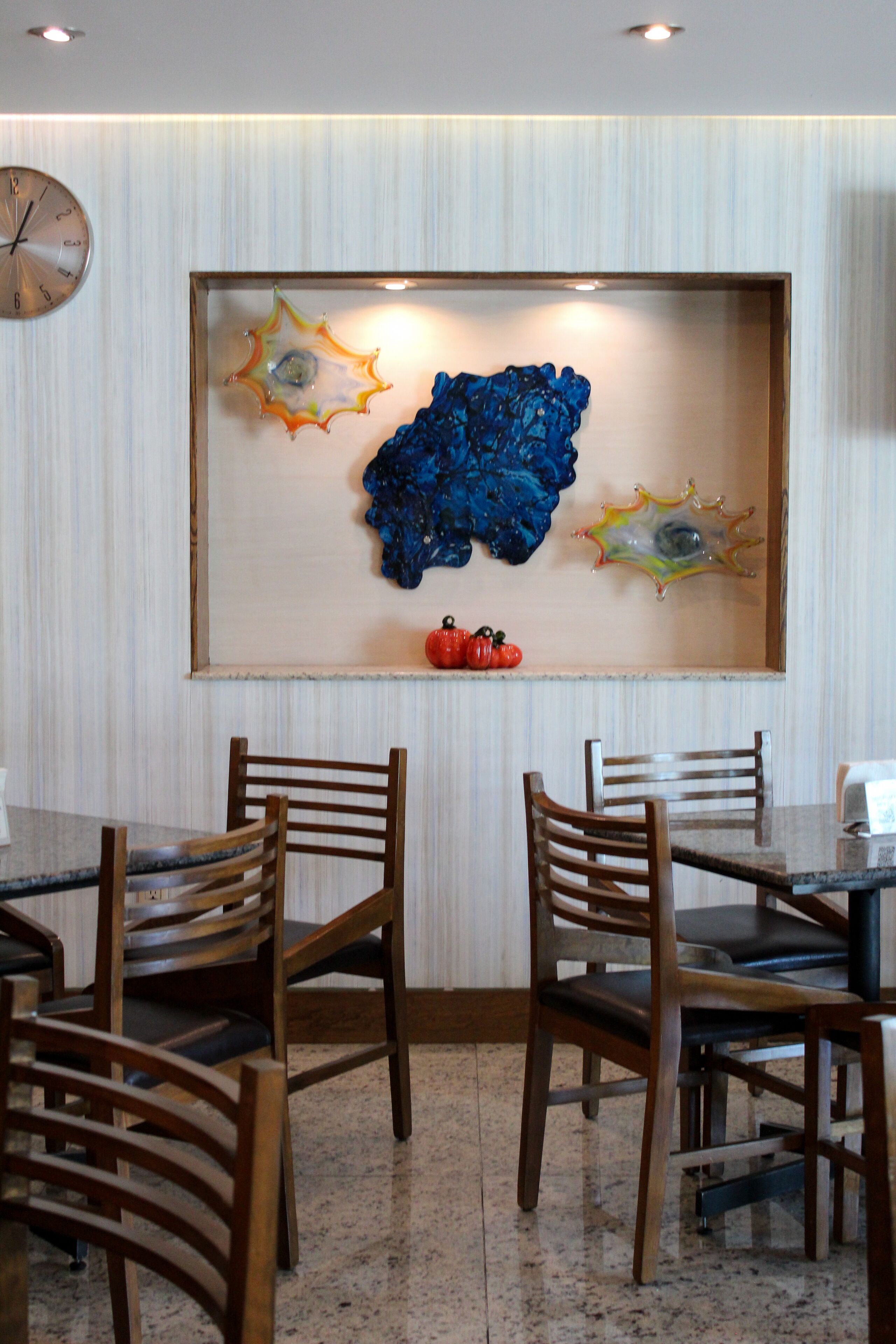 Un comedor con una mesa y sillas, un reloj en la pared y una obra de arte de vidrio decorativa.