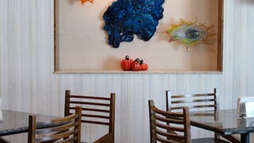 Un comedor con una mesa y sillas, un reloj en la pared y una obra de arte de vidrio decorativa.