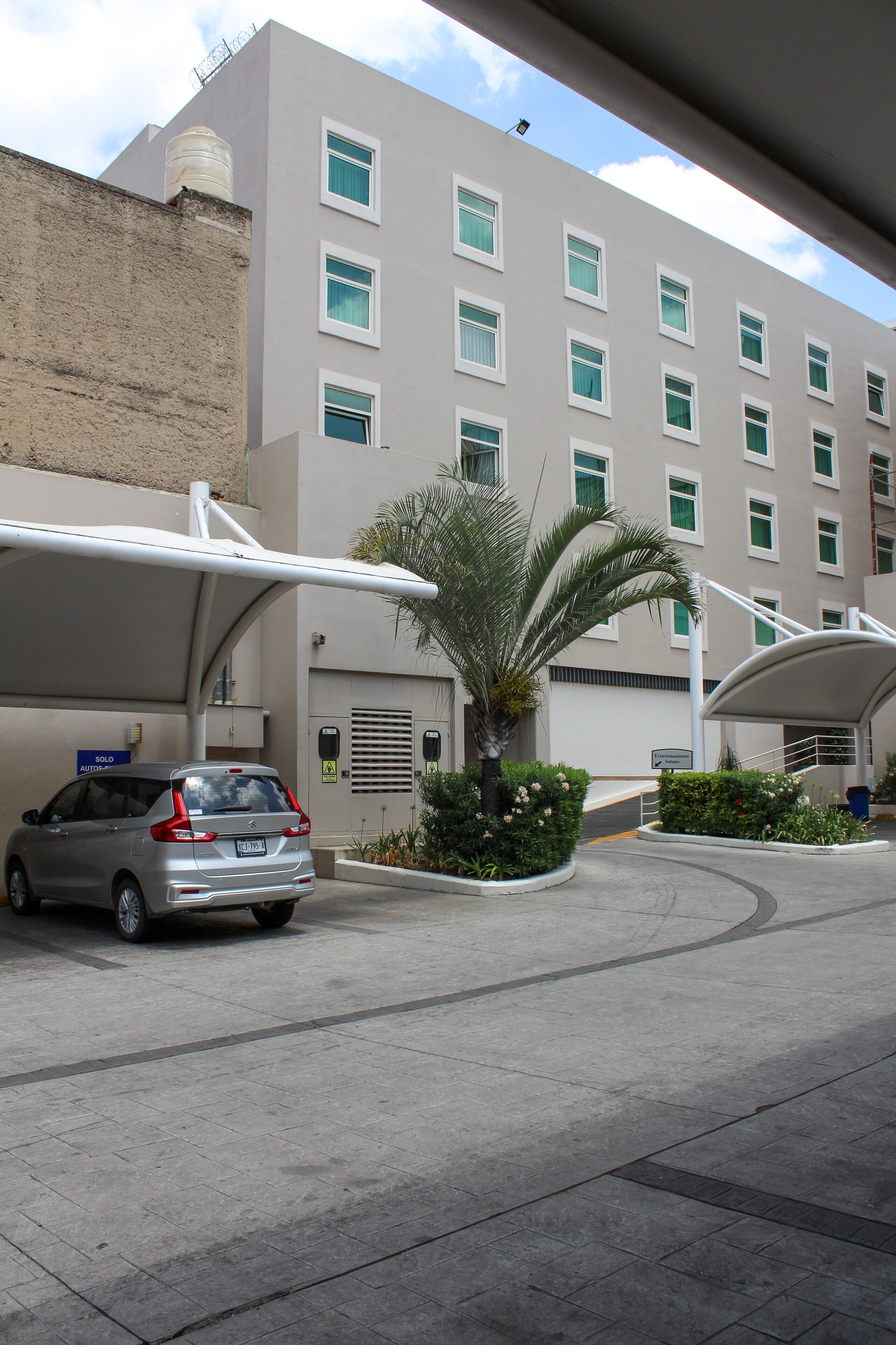 A modern building with a parking area, a covered car parking area, and a palm tree.