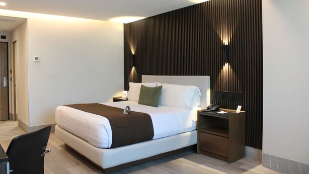 Una habitación de hotel moderna con una cama grande, mesitas de noche, un escritorio y una silla.