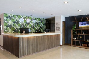 A reception desk with a clock, a flat-screen TV, and a wooden shelf with decorative items. - Hotel Portobelo (Guadalajara)