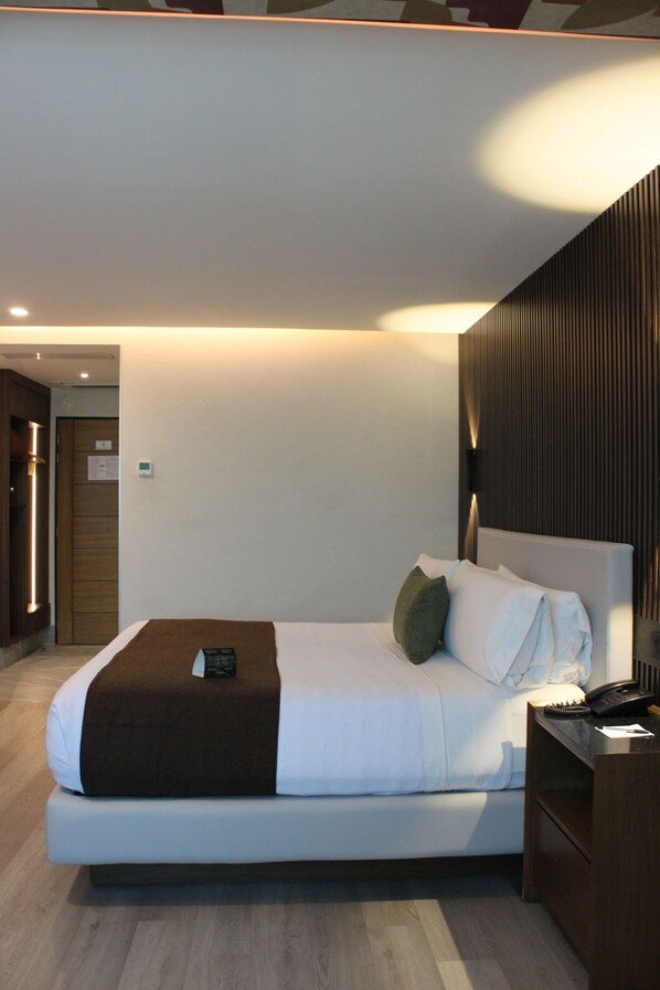 Una habitación de hotel moderna con una cama grande, una mesita de noche y una lámpara de pared.