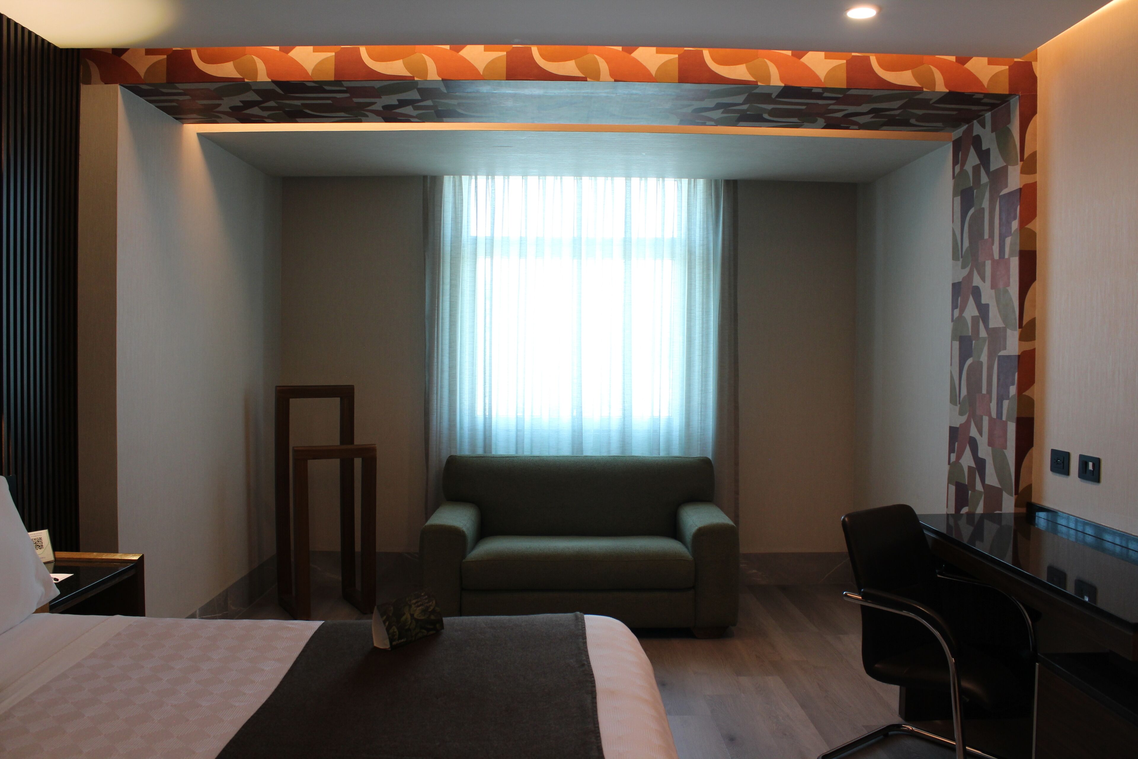 A hotel room with a bed, a sofa, a desk, and a window with curtains.